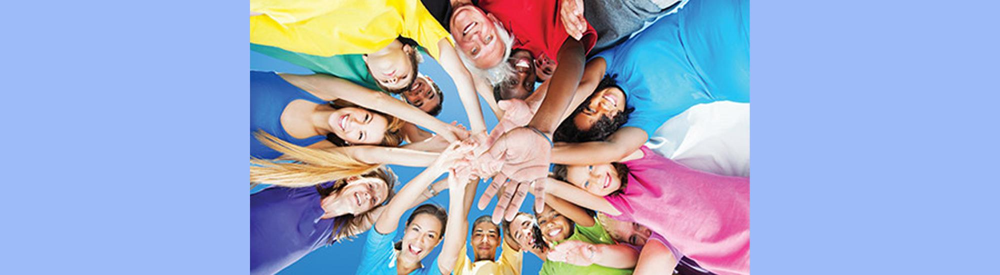 Circle of people with arms extended and hands together looking at camera.